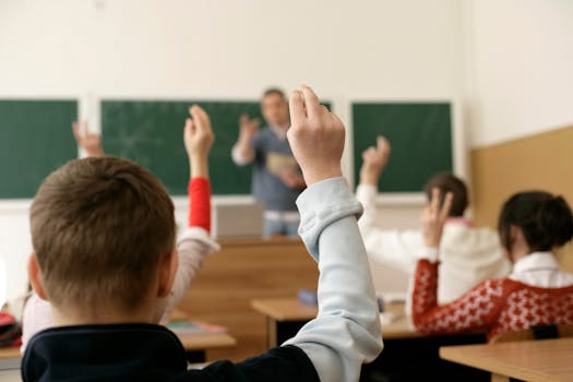 Students in a classroom raising hands, engaging in a lesson with the teacher.